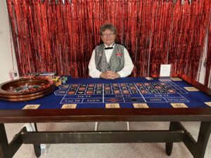 A man sitting behind a casino table wearing a grey waistcoat and a black bow